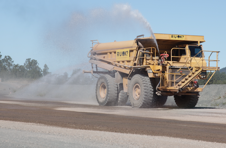 a vehicle moving along at a mine site spraying water onto the ground